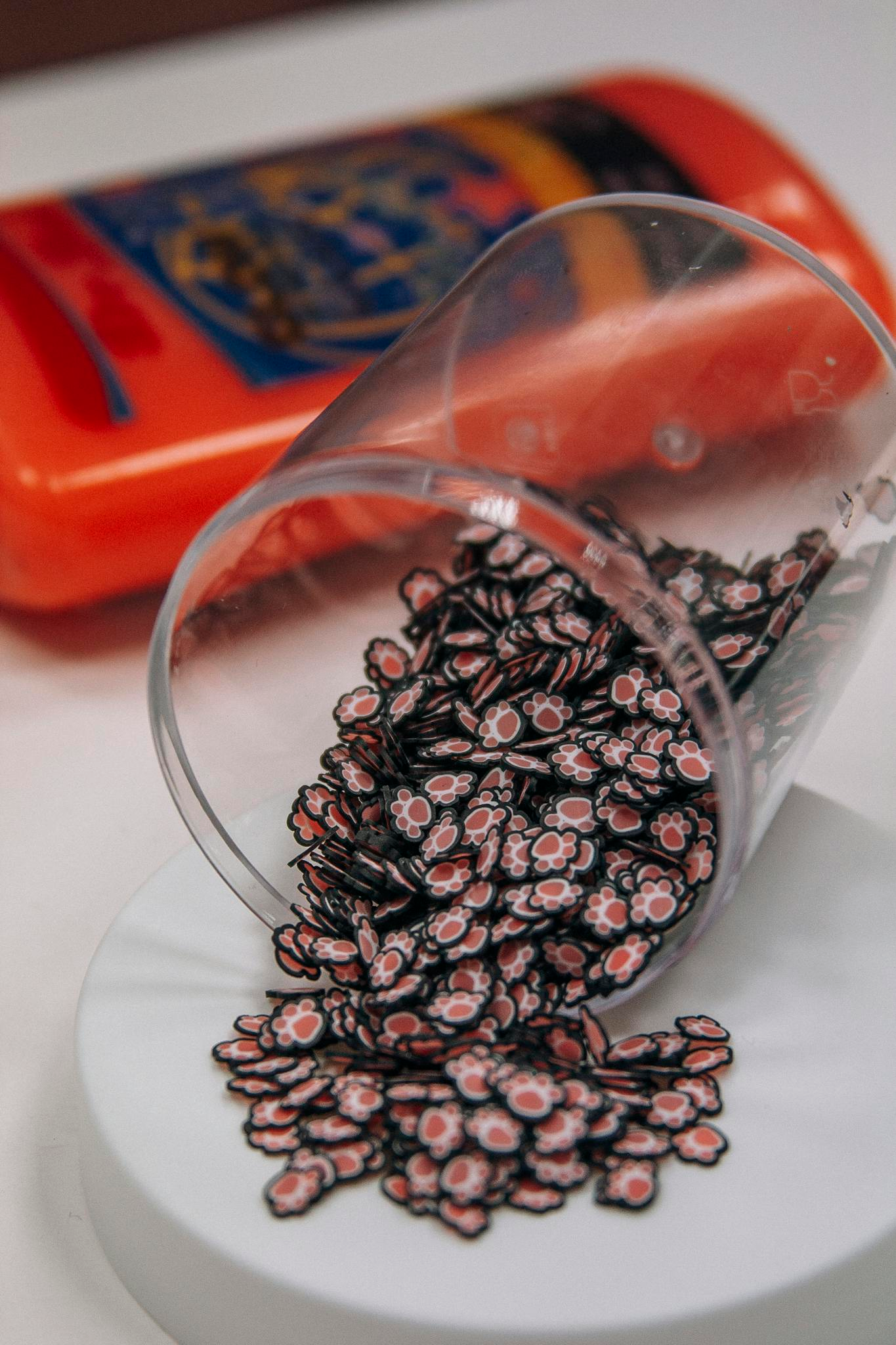 Photo by Oleg Prachuk Charming paw-shaped beads spilling from a transparent cup onto a surface.