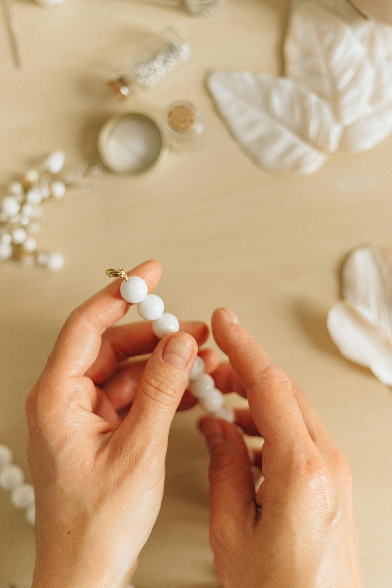Photo by Nataliya Vaitkevich Close-up of hands crafting handmade bead necklace on a wooden surface.