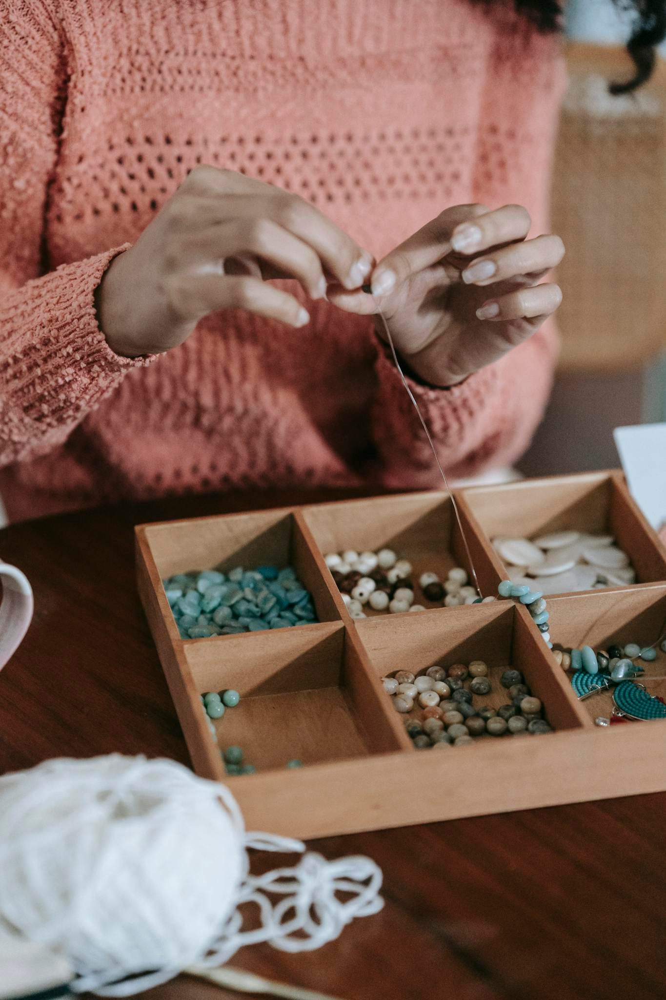 Photo by Miriam Alonso Crop unrecognizable ethnic female in light orange sweater doing beading with colorful beads and fishing line